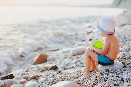 a child on a rock on the beach looking at the oncoming waves at sunsetの写真素材