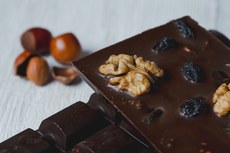 chocolate bar filled with different berries and nuts without heat treatment lie old wooden table with cracked paint on the surface.scattered seeds,Seeds, spices, nuts,buckwheat, and grated cinnamon. rustic styleの写真素材