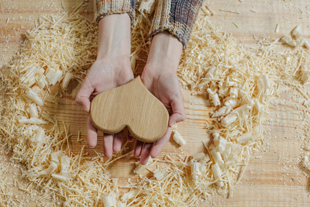 A wooden heart in the gentle hands of a girl on a wooden bench among the sawdust. Handmade on wood
vintage carpentry tools. woodworking, craftsmanship and handwork concept, flat layの写真素材