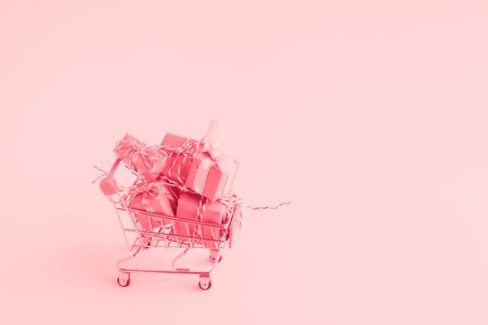 Trolley shopping cart filled with a lot of paper wrapped gift boxes on light background. Toned with pink color. Concept of online shopping. Copy Space for your text.の写真素材