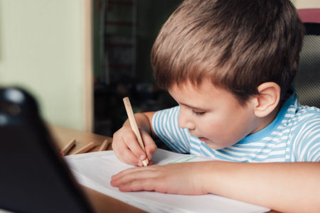 Litle child siting at desk and drawing letters album with colored pencils, lifestyle