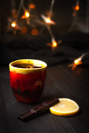 A cup of tea with lemon and chocolate on a dark background with Christmas lightsの写真素材