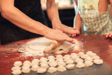 man rolls out the dough for dumplings. Child nearby helps. Close-upの写真素材
