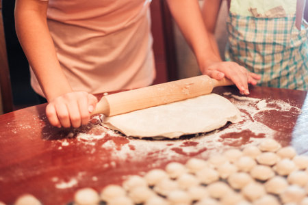 man rolls out the dough for dumplings. Child nearby helps. Close-upの写真素材