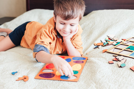 Cute child boy collects wooden puzzle in the form of Easter eggs on bed