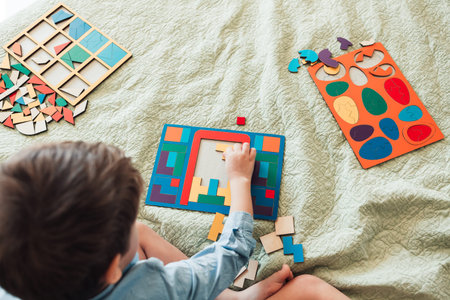 The happy boy sits on the bed and lays puzzles. View from above
