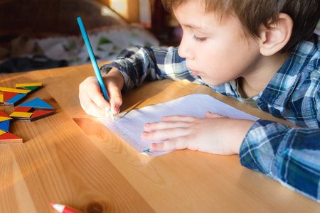 Little child sits by desk and doing lessons, boy writes letters in notebook