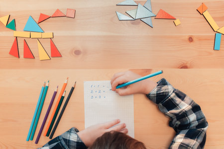 Little child sits by desk and doing math lesson, top view