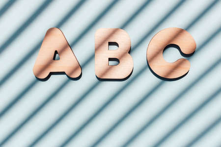 Inscription ABC made from wooden letters. The concept of the importance of education. Blue background with diagonal shadows.の写真素材