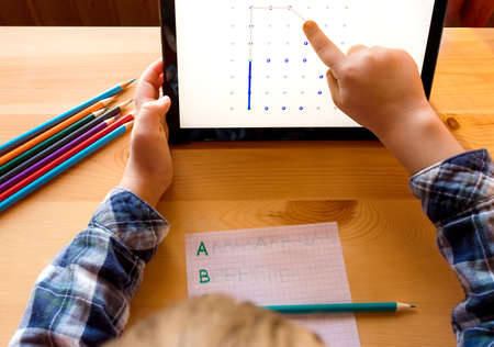 Modern child uses app on tablet to study and draw at home, distance learningの写真素材
