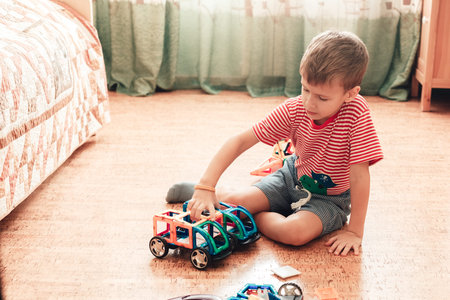 A boy plays with magnetic constructor in children room sitting on cork floorの写真素材