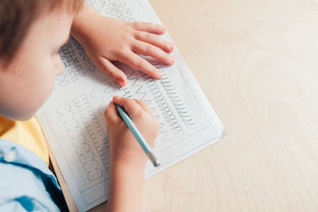 Close up of cute boy doing his homework. Child writing with pencil. Prewriting practice to prepare hands for write letters. Children education conceptの写真素材