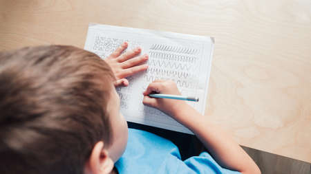 Child boy writing different lines with pencil. Prewriting practice to prepare hands for write letters. Children education concept. View fron aboveの写真素材