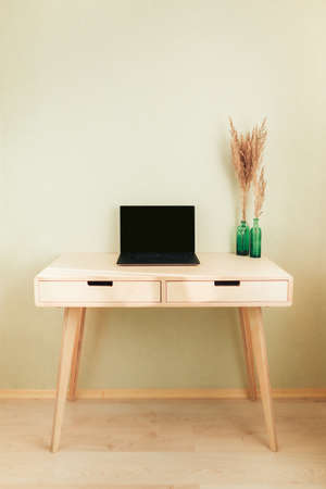 Black laptop on wooden table in home interior. Empty wall with copyspace. Stylish minimalistick workplaceの写真素材