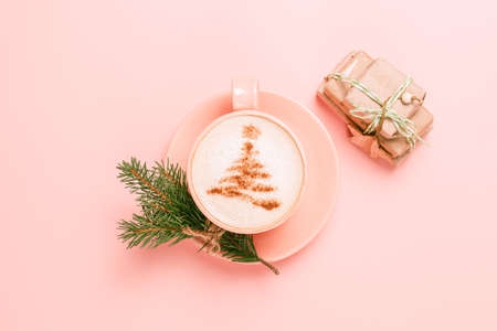 Top view of cup of latte with art in shape of Christmas tree on pink background with branch of fir tree and gift box. Copy space for your textの写真素材