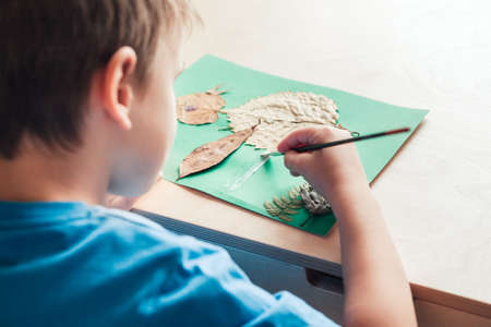 child glues an applique made of autumn leaves, view from backの写真素材