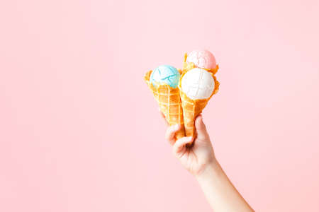 Female hand holding three waffle cones with Christmas balls against pink background, copy spaceの写真素材