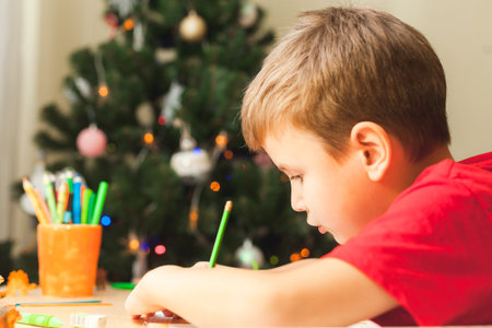 7 yeas old boy sitting at desk and studing. Child write notes in notebook, close up, side view....