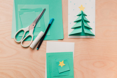 Step 1 of making Christmas card. Sample card, a stack of colored paper of different sizes, scissors and glue. Preparing to make a postcard by a childの写真素材