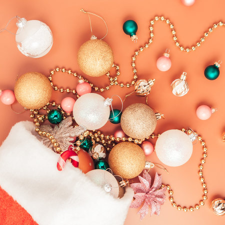 christmas decorations fall out of santa hat on orange background, top view, close up