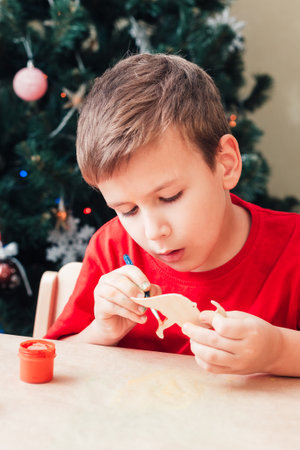 Cute 7 years old child boy paints wooden dinosaur toy for Christmas treeの写真素材