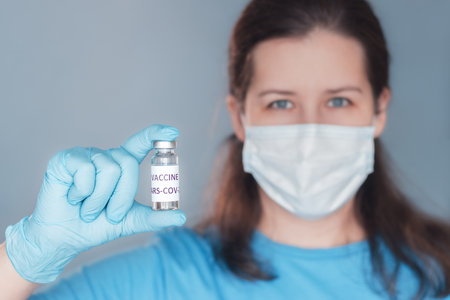Young woman holds vial of vaccine in hand. Focus on hand with bottleの写真素材