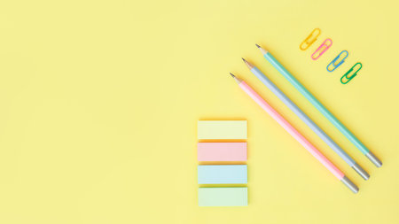 office supplies on a yellow background with copy space. Graphite pencils, paper clips and sticky...