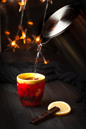A cup of tea with lemon and chocolate on a dark background with Christmas lights. A cup of tea poured from A cup of tea poured from electric kettleの写真素材
