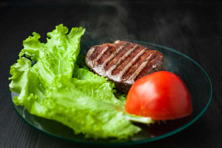 Hot piece of roasted meat on a plate with vegetables on a dark backgroundの写真素材