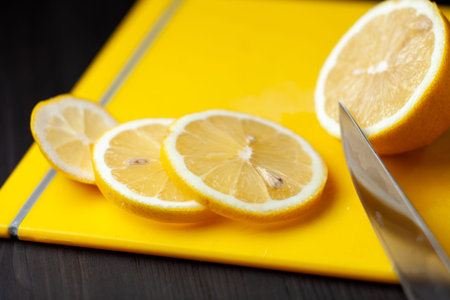 Sliced lemon on yellow cutting board and knife next to it