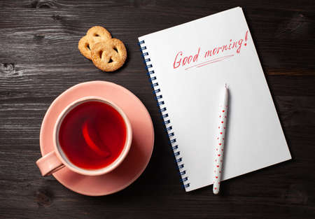 Open copybook with inscription good morning, a cup of pomegranate tea, a pen on a black wooden backgroundの写真素材