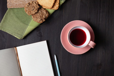 A book, cup of pomegranate tea, pen and cookies on a plate on a green towel. Breakfast conceptの写真素材