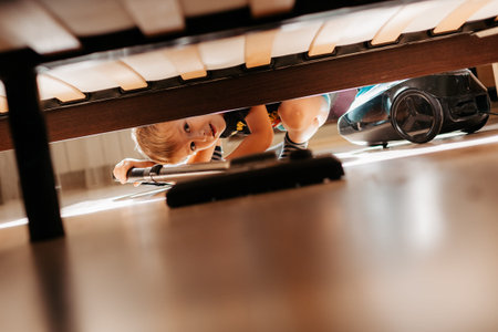 Little child using vacuum cleaner at home. Cute boy cleaning floor in bedroomの写真素材