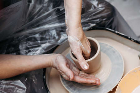 Close up of woman hands molding clay mug spinning on pottery wheel. Potter hands forming clay cup spinning on pottery wheel on pottery workshopの写真素材