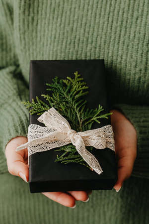 Female hands holding nice gift box. Woman giving wrapped in black paper present. Cozy gift wrapping designの写真素材
