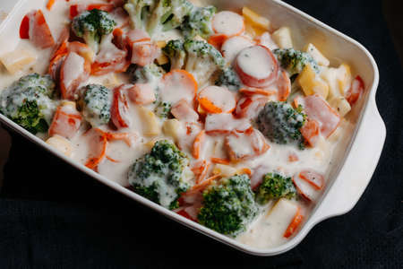 Sliced vegetables in a white ceramic bowl with grated cheese and sauce. Preparation of baked vegetables. Close up viewの写真素材