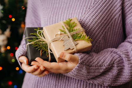 girl hands holding small gift in her hands. Close up. decorated Christmas tree on background. Bright Christmas card with space for text with space for textの写真素材