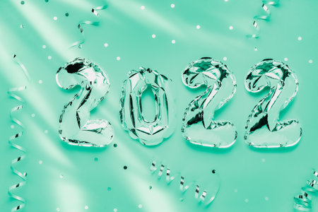 Foil balloons in form of numbers 2022. Silver color air balloons on green background. Flat lay with copy spaceの写真素材