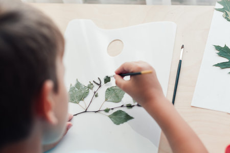Close up of child sitting at desk and making picture from dry birch leaves. Autumn activities for childrenの写真素材