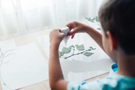 Close up of child sitting by desk and making picture from dry birch leaves. Autumn activities for childrenの写真素材