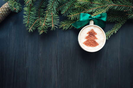 Top view of cup of cappuccino with milk foam topped with cocoa power. Latte art. Dark wooden background. Coffee mug hanging on fir tree as Christmas ballの写真素材