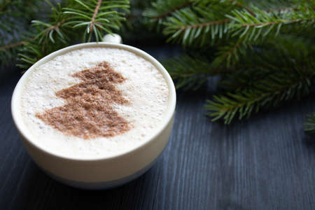 Side view of cup of cappuccino with milk foam topped with cocoa power. Latte art. Dark wooden background and fir treeの写真素材