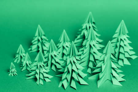 Several paper Christmas trees made using the origami technique on a green paper background. Forest conservation conceptの写真素材