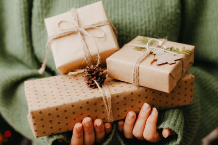 Closeup of woman in green pullover holding many gift boxes in her hands. Close up. Gift boxes wrapped in craft paperの写真素材