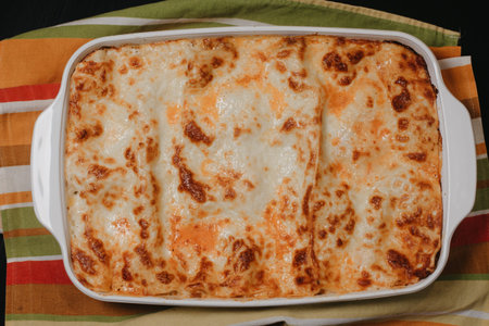 Homemade lasagna in a white bowl on a green kitchen towel, top view