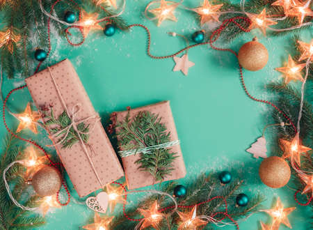 Two Christmas gift boxes wrapped in craft paper on light green background with branch of fir treeの写真素材