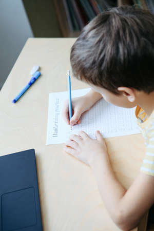 Top view to cute boy doing his homework. Child writing with pencil. Writing practice lettersの写真素材