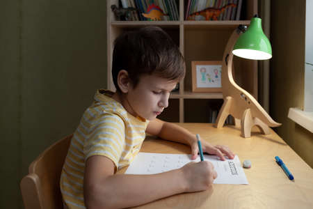 A schoolboy doing math lesson sitting at desk in the children room, side viewの写真素材