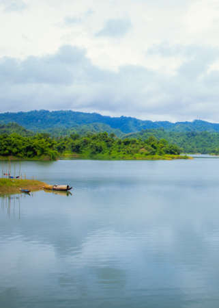 Beautiful landscape of a lake which is surrounded by green mountains with cloudy sky. A boat resting onshore. In Rangamati, Bangladesh.の写真素材