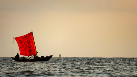 A traditional wooden fishing boat with a vibrant red sail drifts across the Bay of Bengal, Bangladesh. Showcasing the timeless charm of coastal life.の写真素材